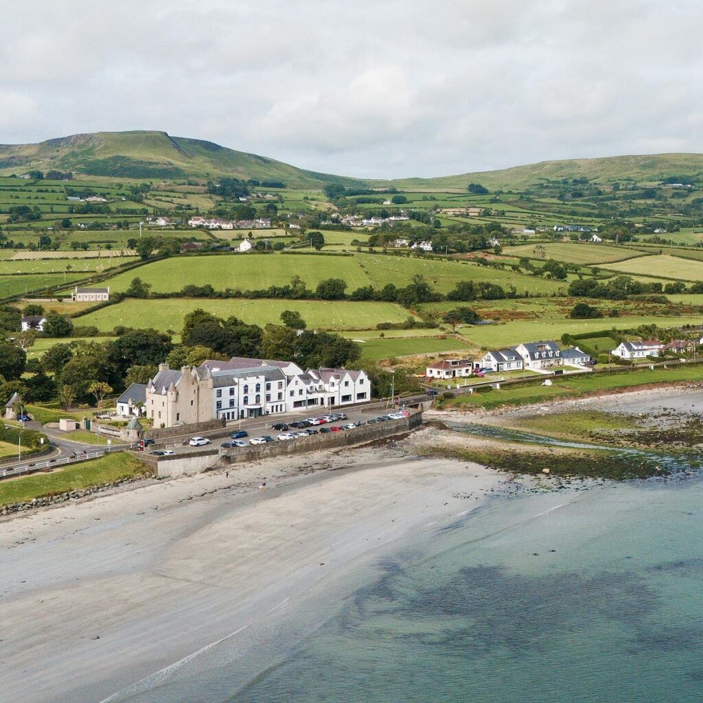 Coastal village with beach and green hills in the background, featuring houses and countryside landscape.