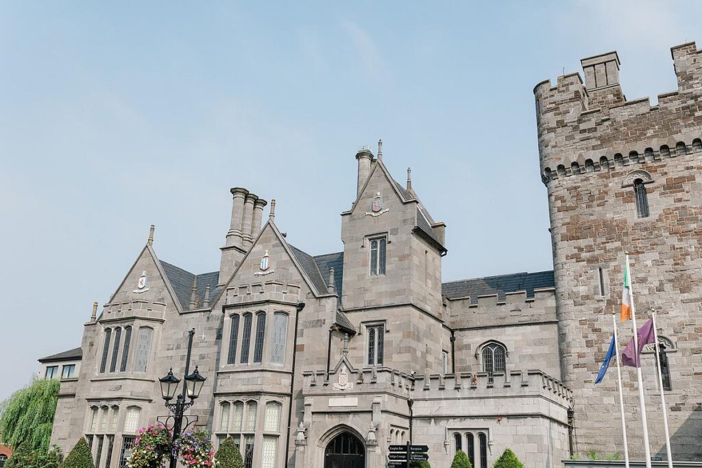 Historic stone castle with flags flying, featuring gothic architecture against a clear blue sky.