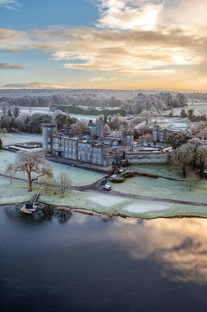 Aerial view of a historic castle surrounded by frosty landscape and lake at sunrise.