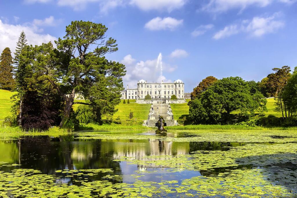 Elegant mansion with garden view, reflecting in a serene lily pond under a clear blue sky.