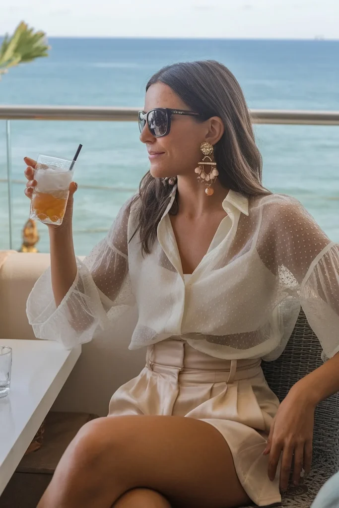 Woman relaxing by the ocean, wearing sunglasses and chic summer outfit, holding a cold drink.