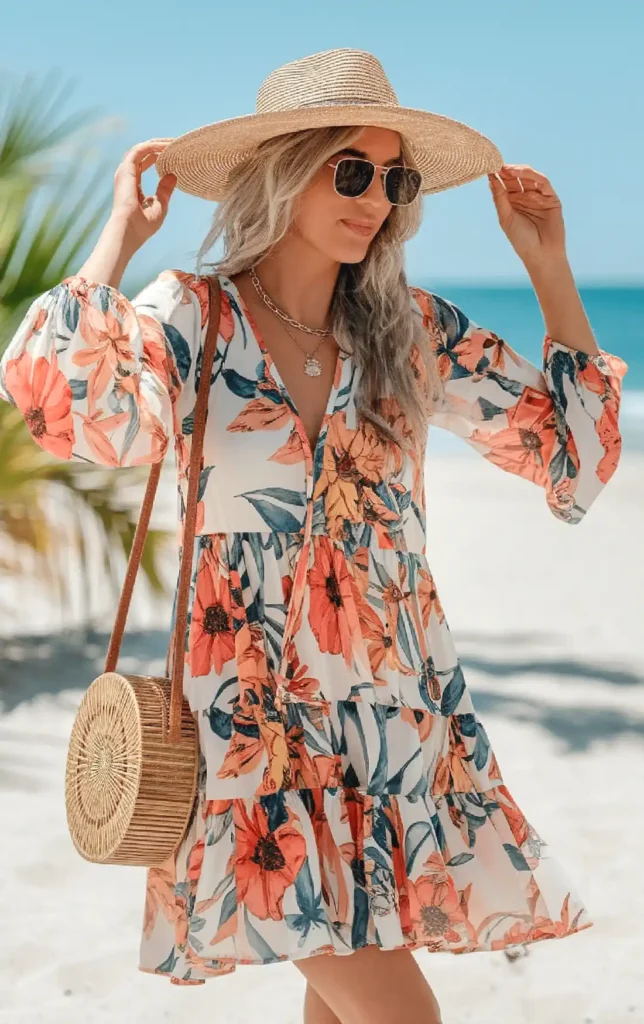 Woman in floral dress and sunhat enjoying a sunny beach day, with ocean in the background.