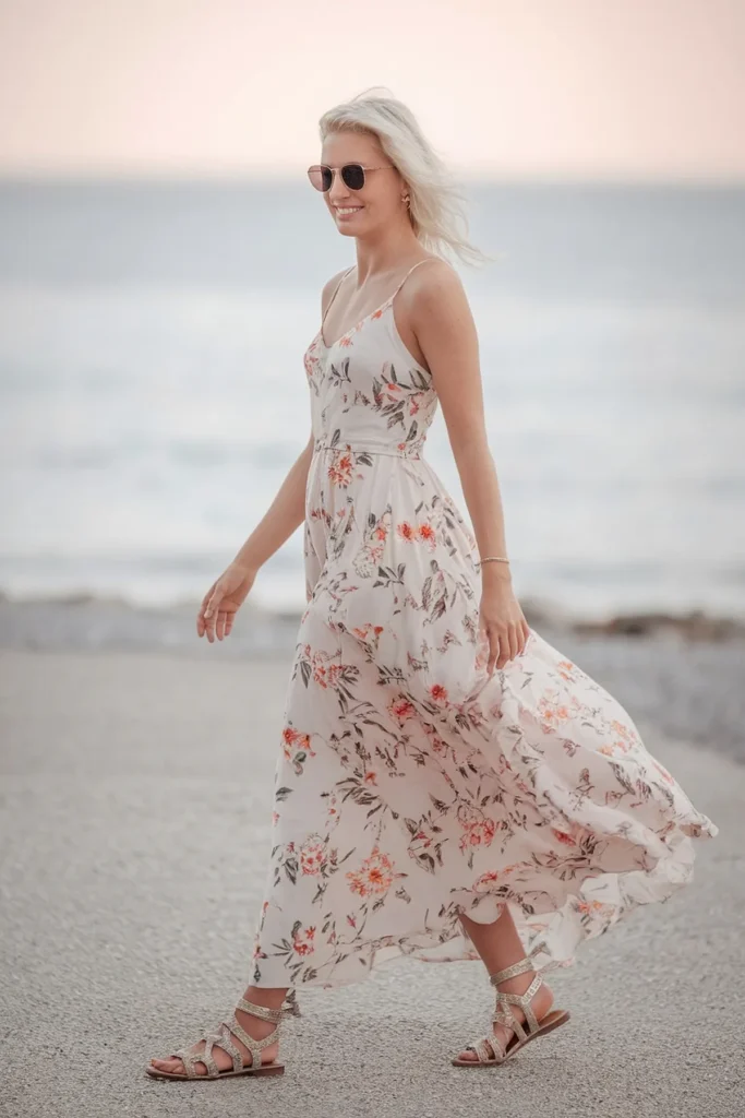 Woman in a floral dress walks on the beach, enjoying a sunny day.