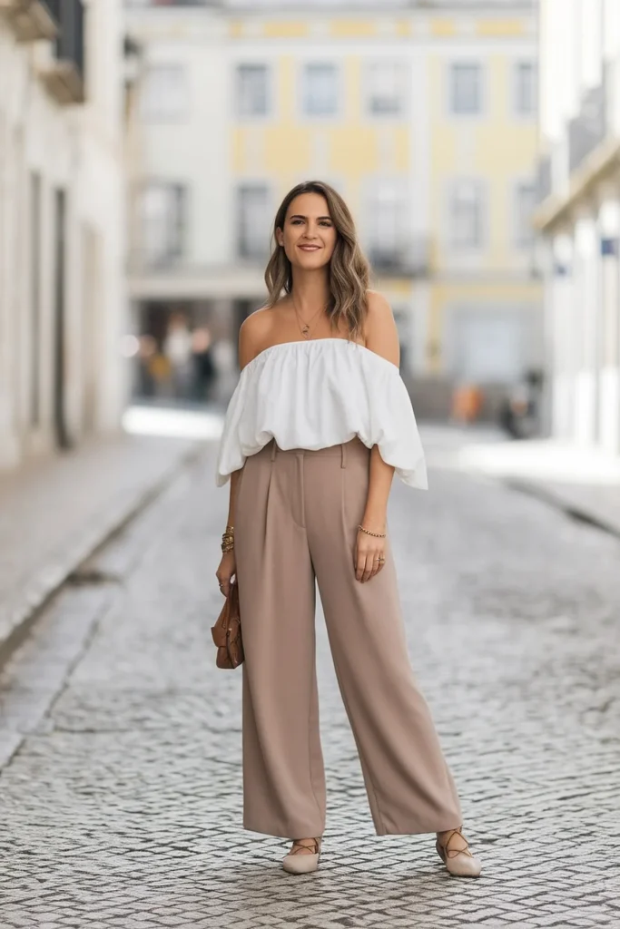 Fashionable woman in stylish off-shoulder top and trousers on a cobblestone street.