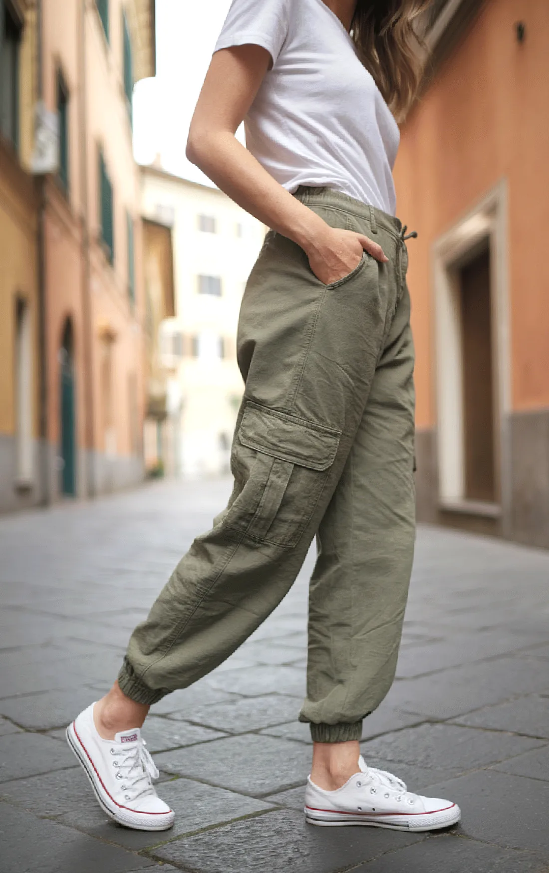 Woman in casual cargo pants and white sneakers walking on a cobblestone street.