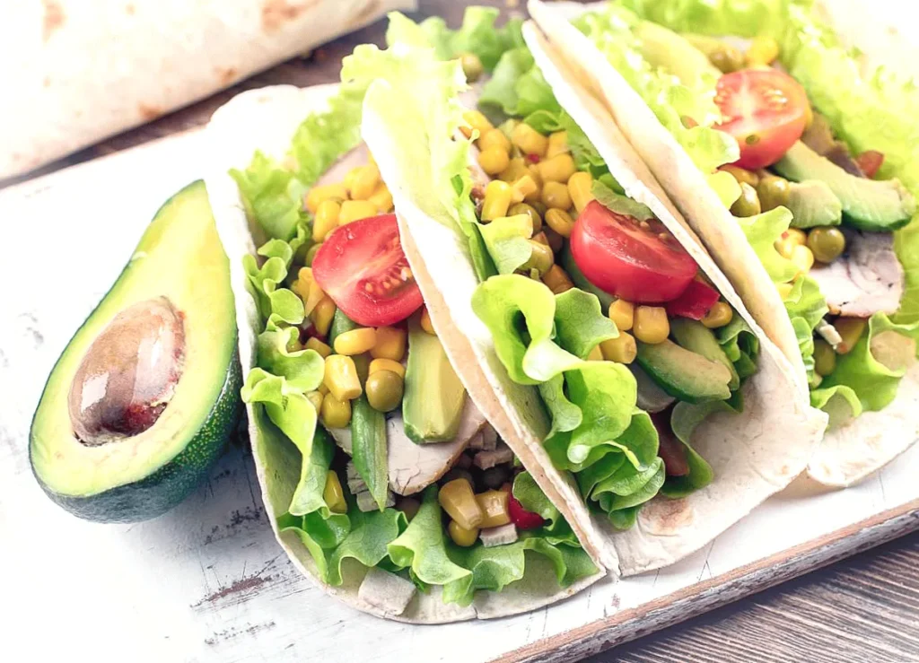 Fresh veggie tacos with avocado, lettuce, tomato, and corn filling on a wooden board.