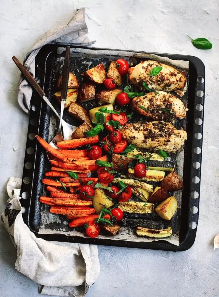 Oven-roasted chicken with seasoned vegetables including carrots, potatoes, and tomatoes on a baking tray.