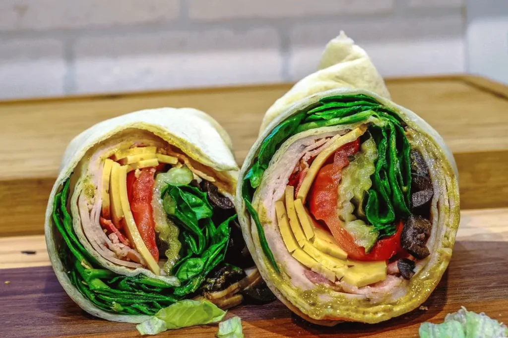 Fresh veggie wrap with lettuce, tomatoes, cheese, and olives on a wooden board, ready to eat.