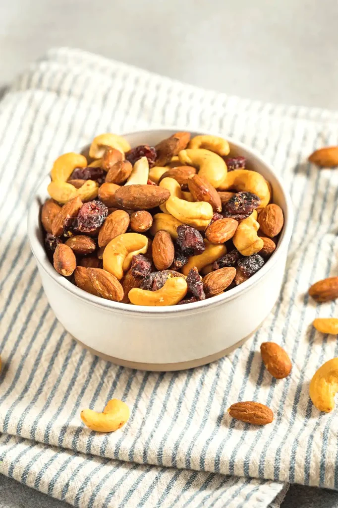 Bowl of mixed nuts including almonds, cashews, and cranberries on a striped cloth, ideal for healthy snacking.