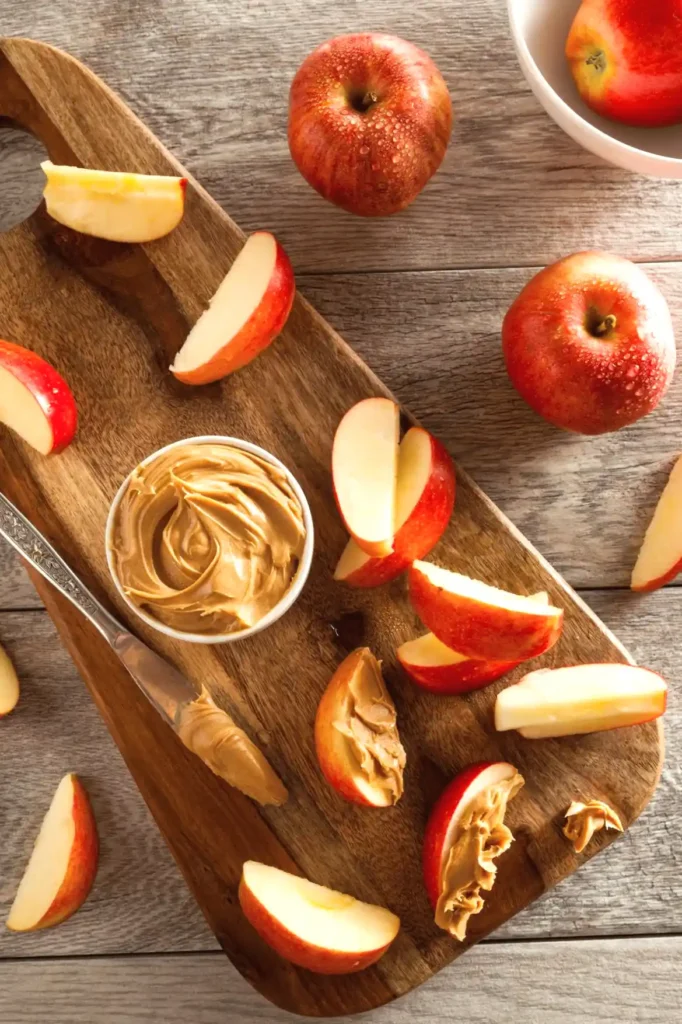 Sliced apples with peanut butter on wooden board, a healthy snack option with fresh apples and creamy spread.