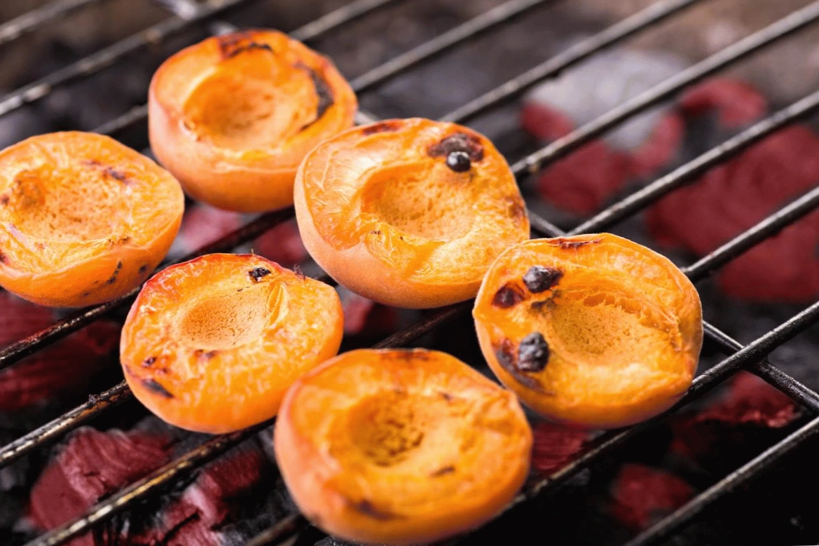 Grilled halved apricots on barbecue grill, showcasing charred edges and vibrant orange color. Perfect summer dessert.