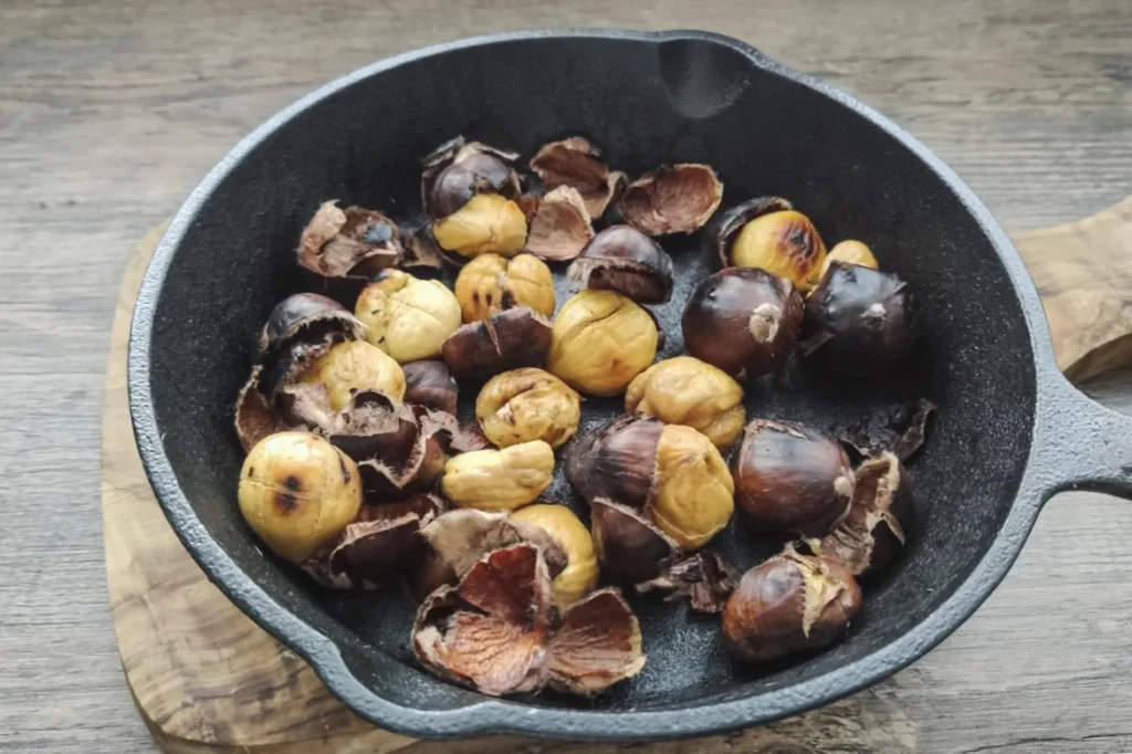 Roasted chestnuts in a black cast iron skillet on a wooden surface, perfect for cozy winter snacks.
