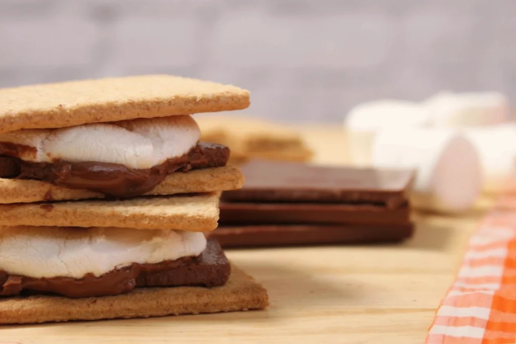 Two delicious s'mores with melted chocolate and marshmallows between graham crackers on a wooden table.