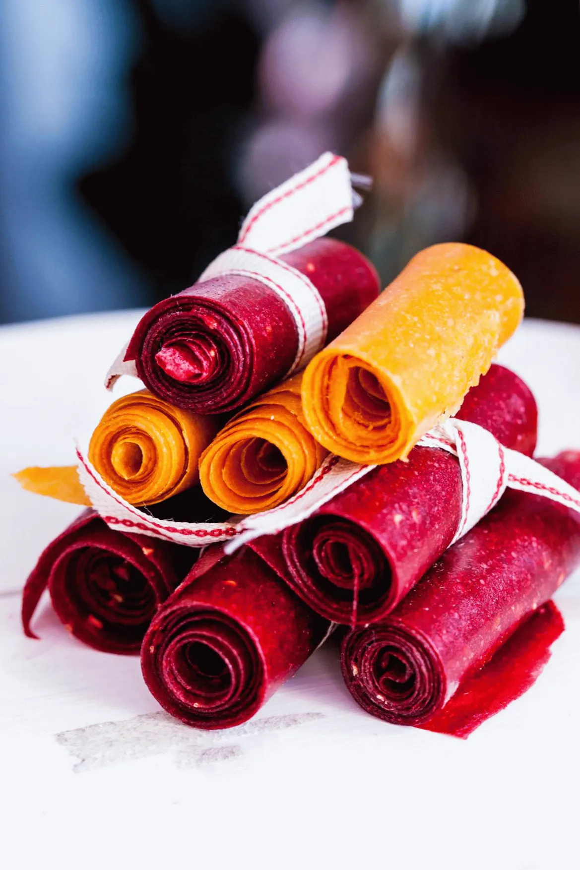 Colorful rolled fruit leathers stacked decoratively on a white surface, tied with ribbon for a vibrant snack display.
