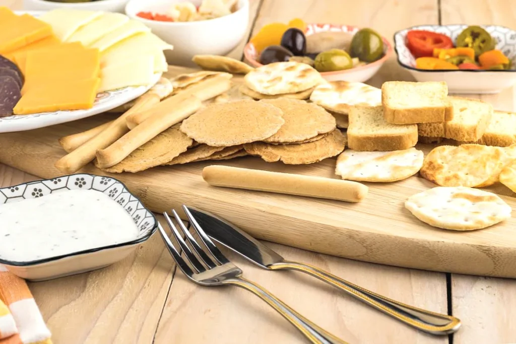 Assorted crackers and cheese platter with dips and olives on a wooden board, ready for a party snack.