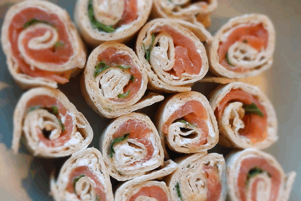 Assorted smoked salmon pinwheels with cream cheese on a platter, perfect for appetizers or party snacks.