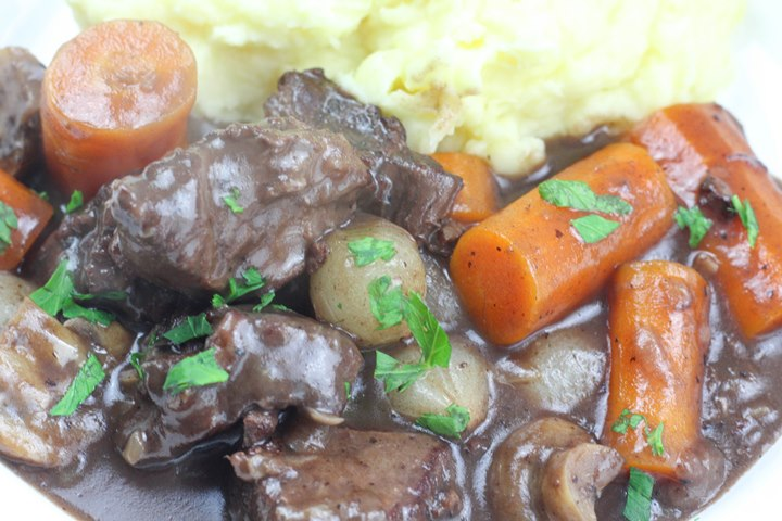 Hearty beef stew with carrots, mushrooms, and mashed potatoes, garnished with fresh parsley. Comfort food dish.