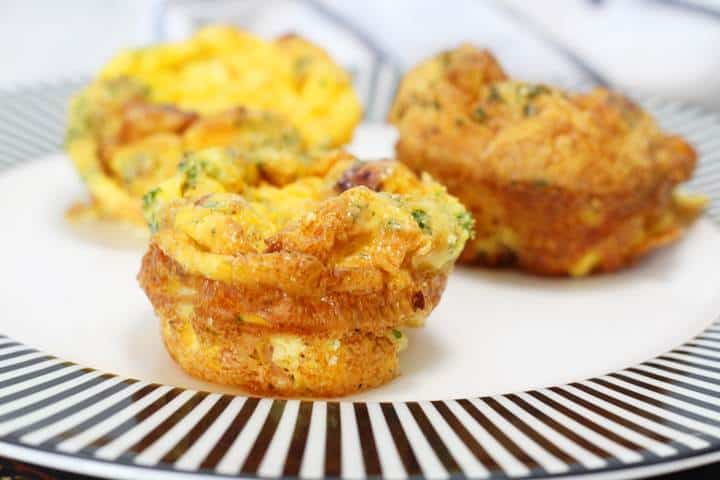 Three fluffy egg muffins with vegetables on a striped plate, perfect for a healthy breakfast or snack.