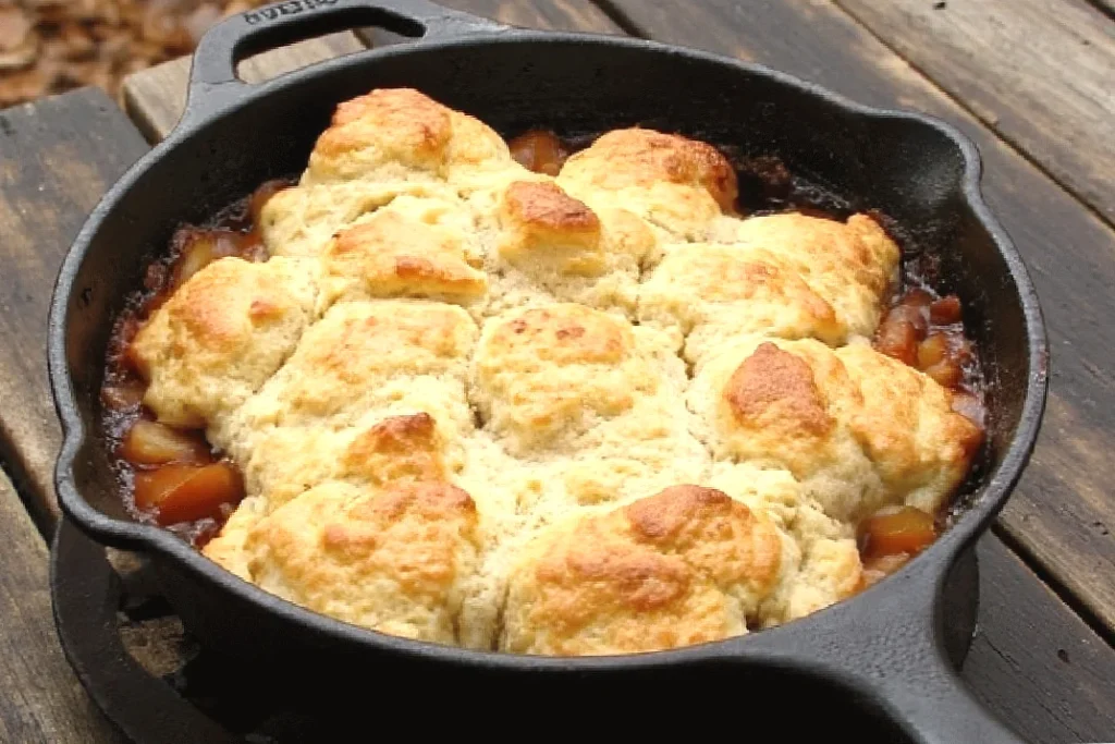 Golden-brown cobbler in a cast iron skillet on wooden surface, highlighting its rustic homemade appeal.