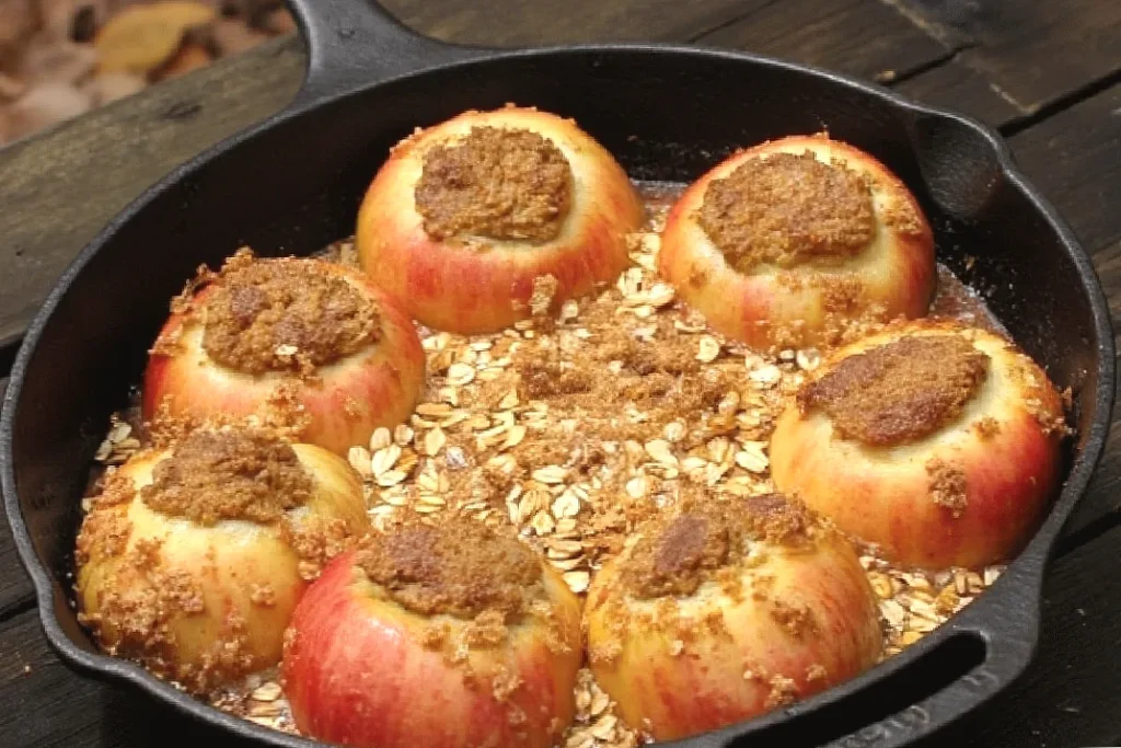 Baked apples topped with brown sugar and oats in a cast iron skillet on a rustic wooden table.