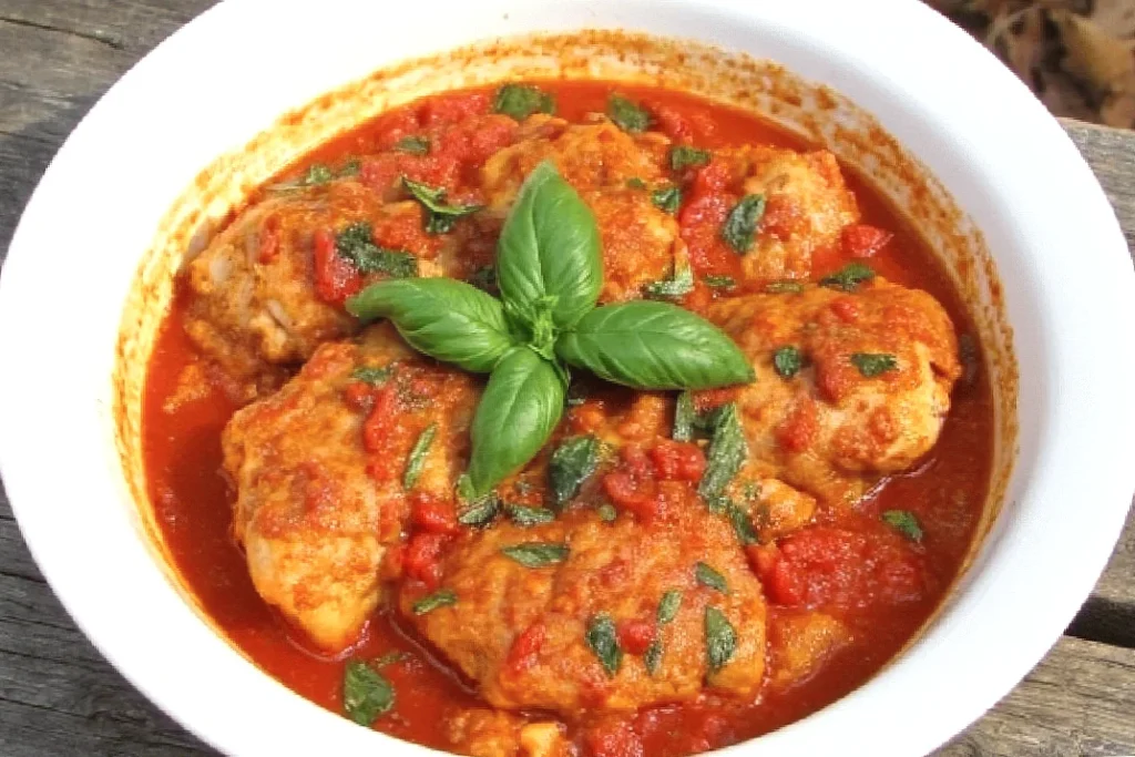 Delicious chicken cacciatore in tomato sauce, topped with fresh basil leaves in a white bowl. Perfect Italian cuisine.