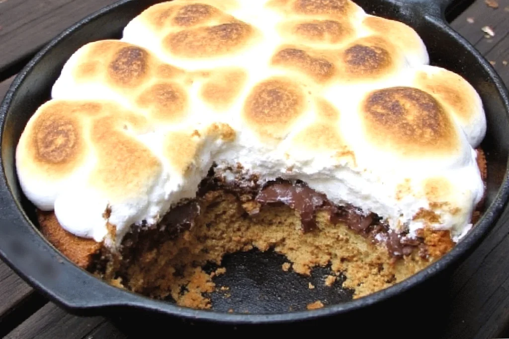 Cozy fall rv meals, Toasted marshmallow s'mores dip in a cast iron skillet with a portion missing, revealing chocolate and graham layers.