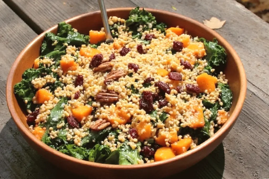 Healthy kale salad with quinoa, sweet potatoes, cranberries, pecans in a wooden bowl on a rustic table.