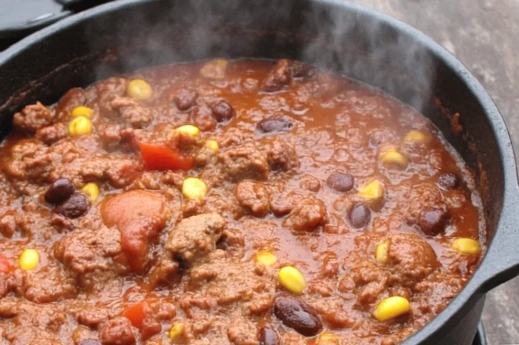 Hearty beef chili simmering with beans and corn in a black pot.