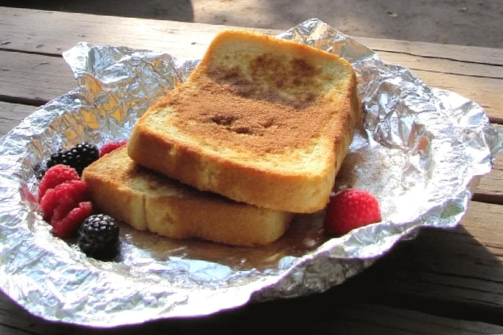 Two cinnamon toast slices with mixed berries on foil, placed on a wooden table, bathed in natural light.