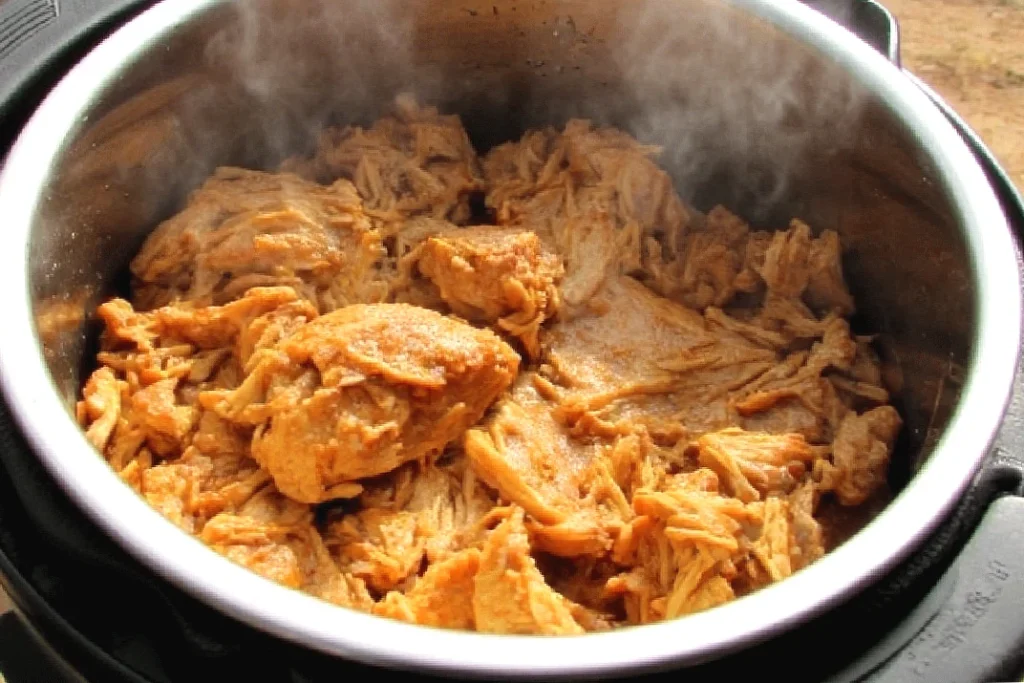 Shredded chicken in a slow cooker, steaming and ready to serve. Perfect for tacos, sandwiches, or a savory meal.