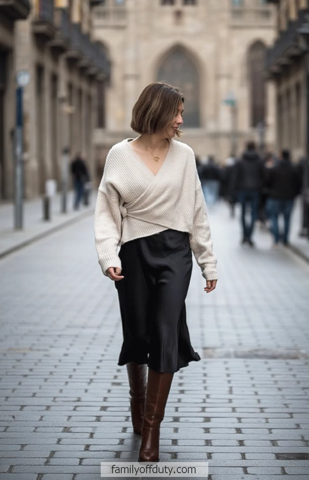 Woman in a cozy sweater and skirt walking down a cobblestone street, blending urban style with casual elegance.