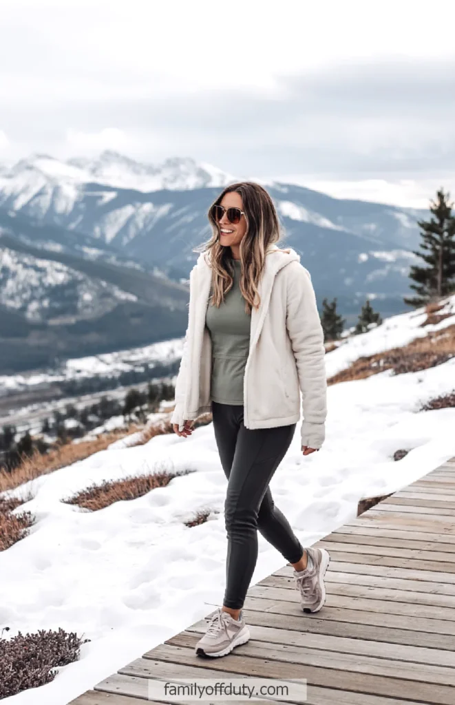 Woman walking on a snowy mountain path, wearing a warm jacket and sunglasses, enjoying the winter landscape.
