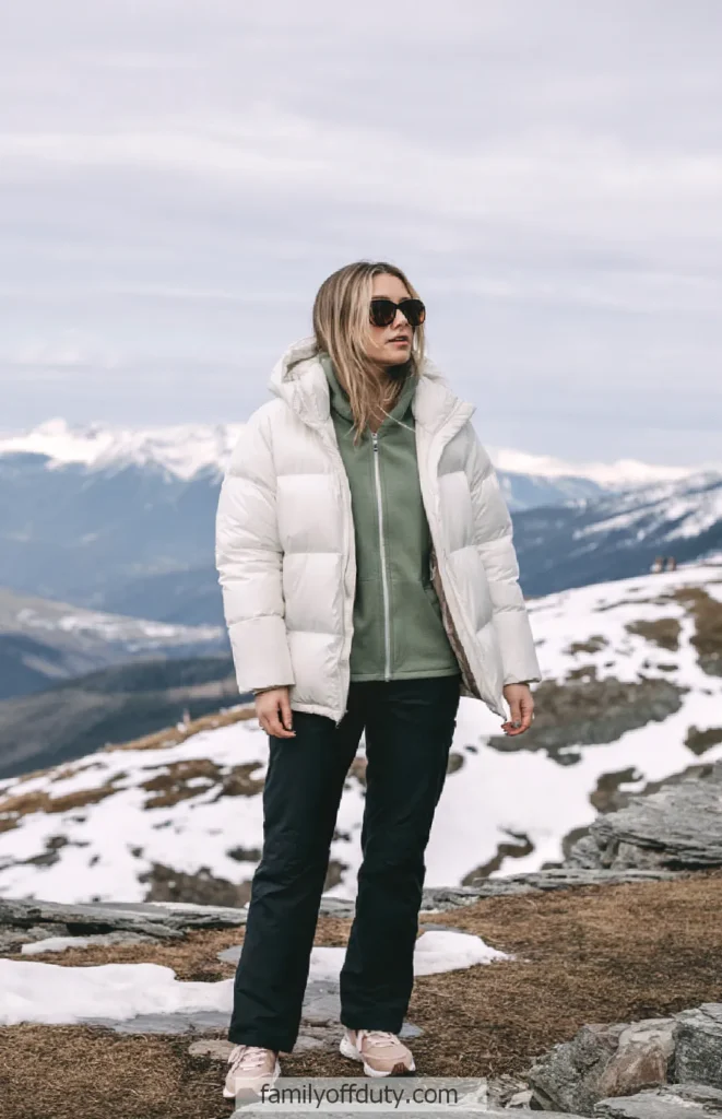 Person in a white puffer jacket and sunglasses standing on a snowy mountain landscape.