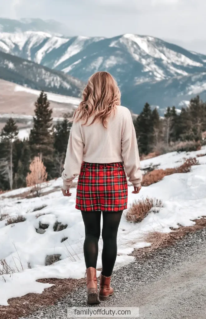 Woman in plaid skirt walks on snowy mountain path, enjoying winter landscape.