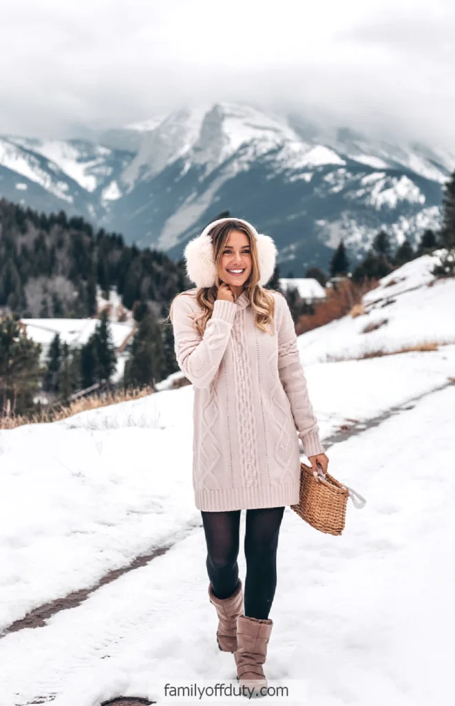 Woman in cozy winter clothes with earmuffs, walking in snowy mountain landscape, holding a wicker basket.