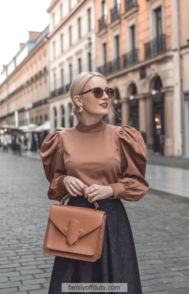 Stylish woman in puff-sleeve top, sunglasses, brown handbag on city street. Trendy fashion and chic urban style.