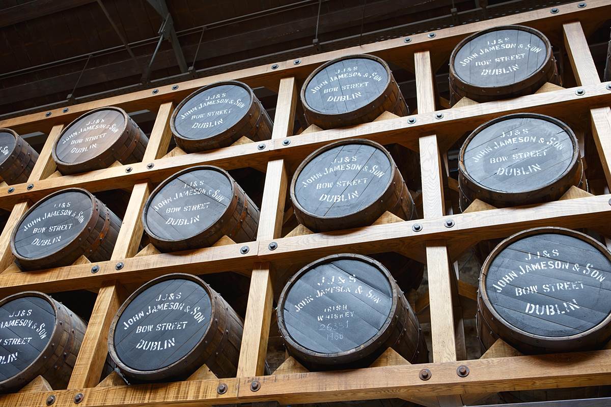 Irish whiskey distillery tours. Whiskey barrels stacked in a distillery warehouse, labeled John Jameson & Son, Bow Street, Dublin.
