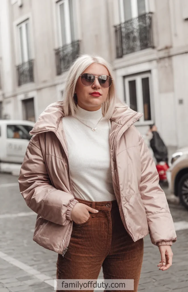 Blonde woman in a stylish pink puffer jacket and sunglasses walking on a city street. Fashionable winter attire.