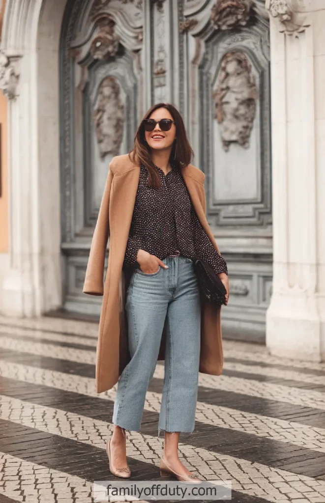 Fashionable woman in stylish outfit with coat and jeans, posing outdoors in front of ornate door.