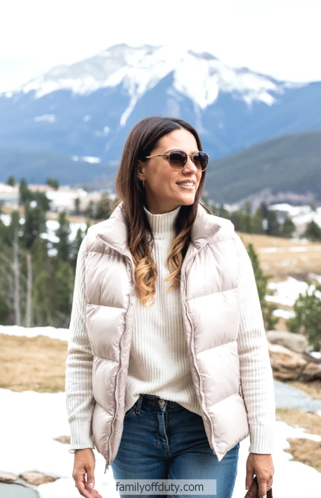 Woman in winter outfit smiling outdoors with snowy mountains in background.