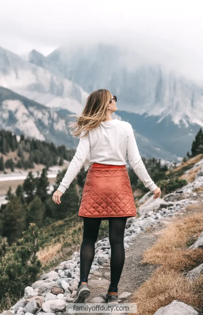 Woman hiking a rocky mountain trail surrounded by pine trees and misty peaks.