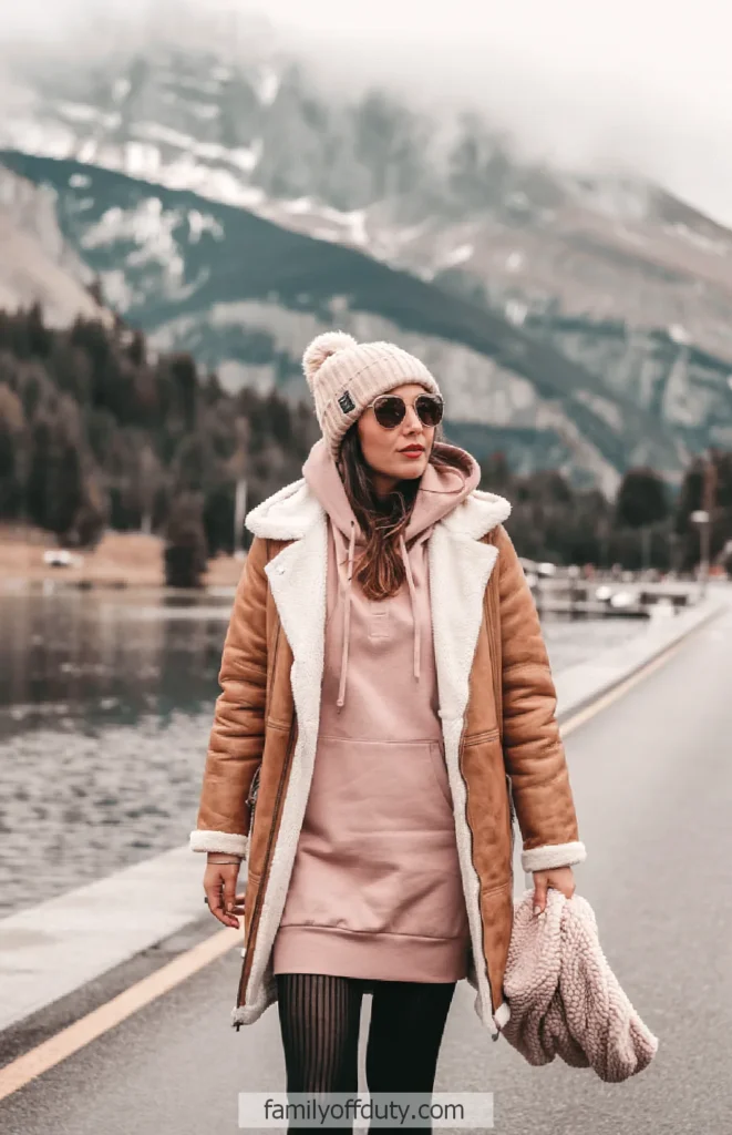 Woman in cozy winter attire walking by a lake with mountains in the background.