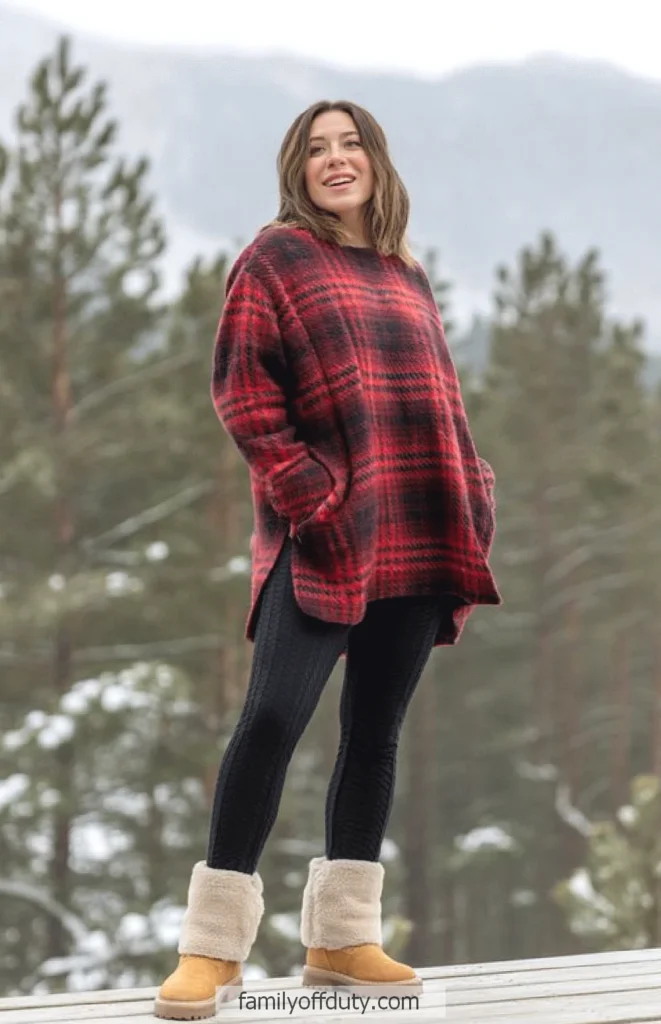 Woman in red plaid sweater and boots enjoys snowy mountain view.