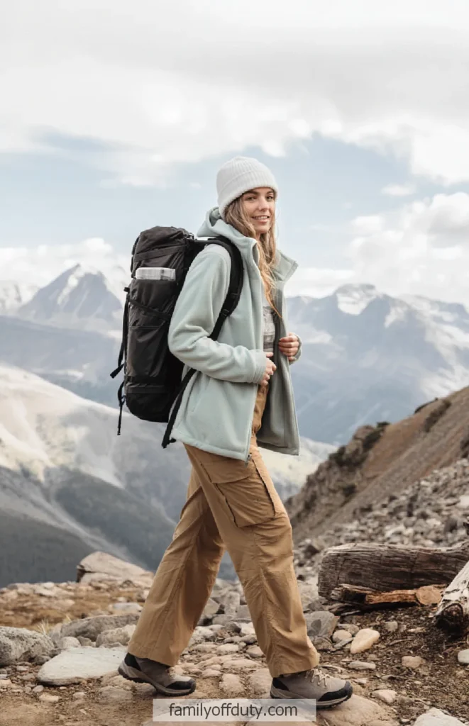 Woman hiking with backpack on mountain trail under cloudy sky.