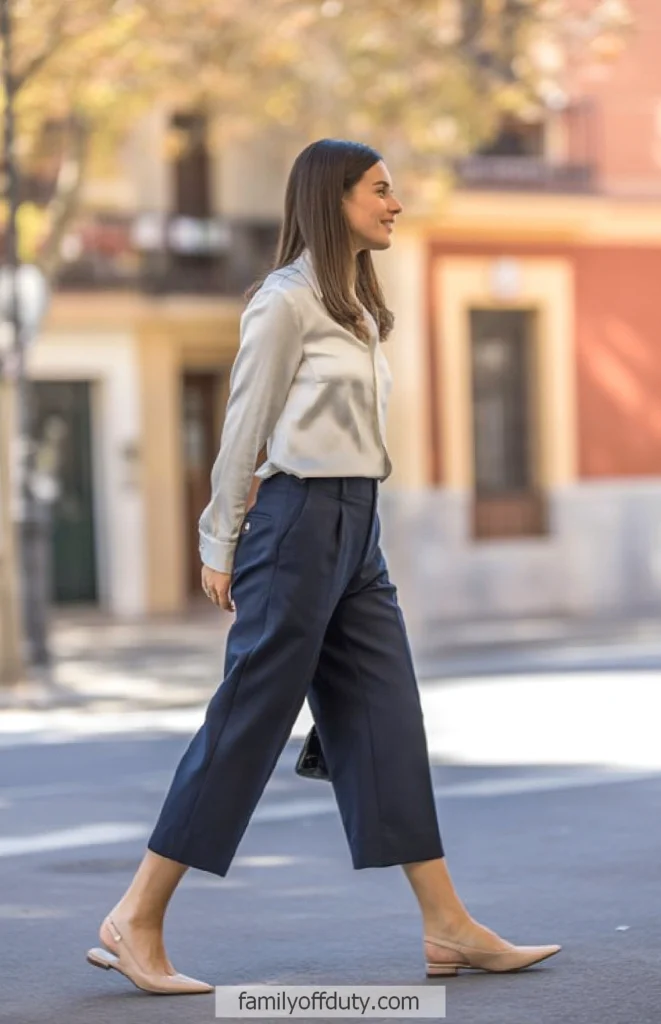 Woman walking stylishly in city, wearing cropped pants and blouse, with neutral flats. Urban fashion scene.