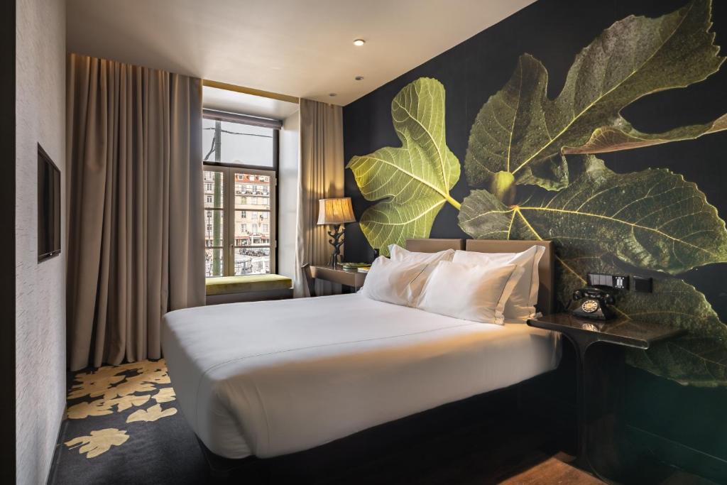Modern hotel room with leafy wallpaper, cozy bed, and urban view through a large window.