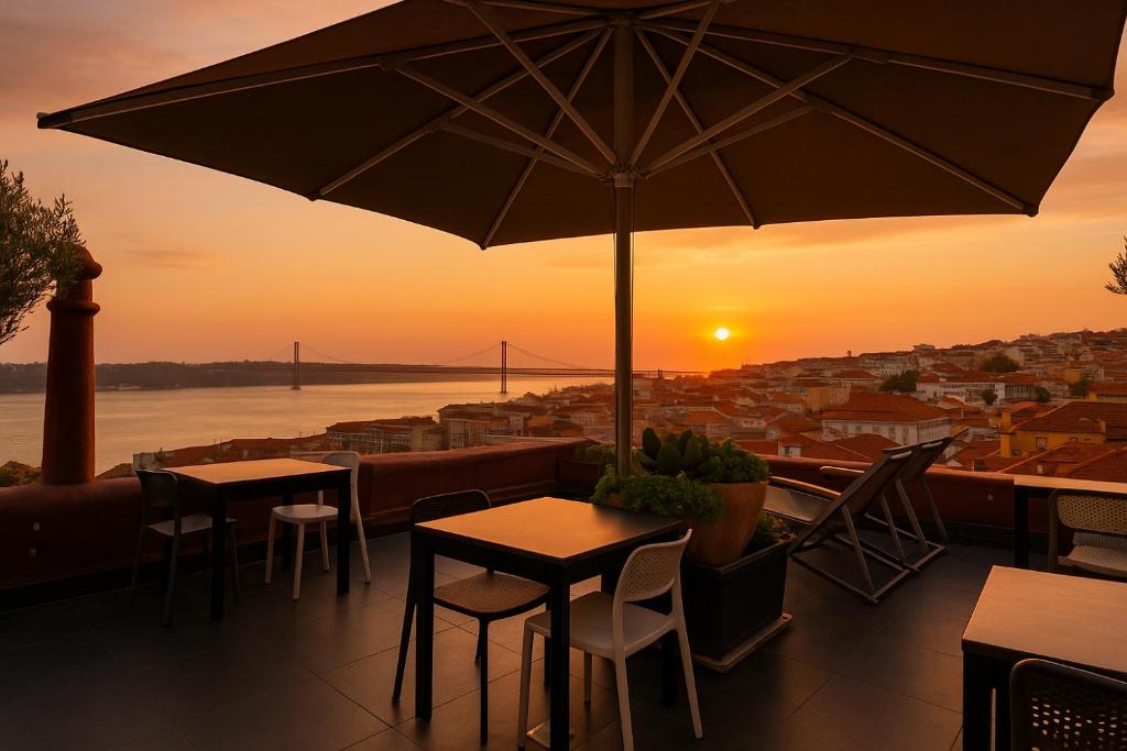 Rooftop patio with tables and umbrella overlooking sunset and cityscape with a bridge in the background.