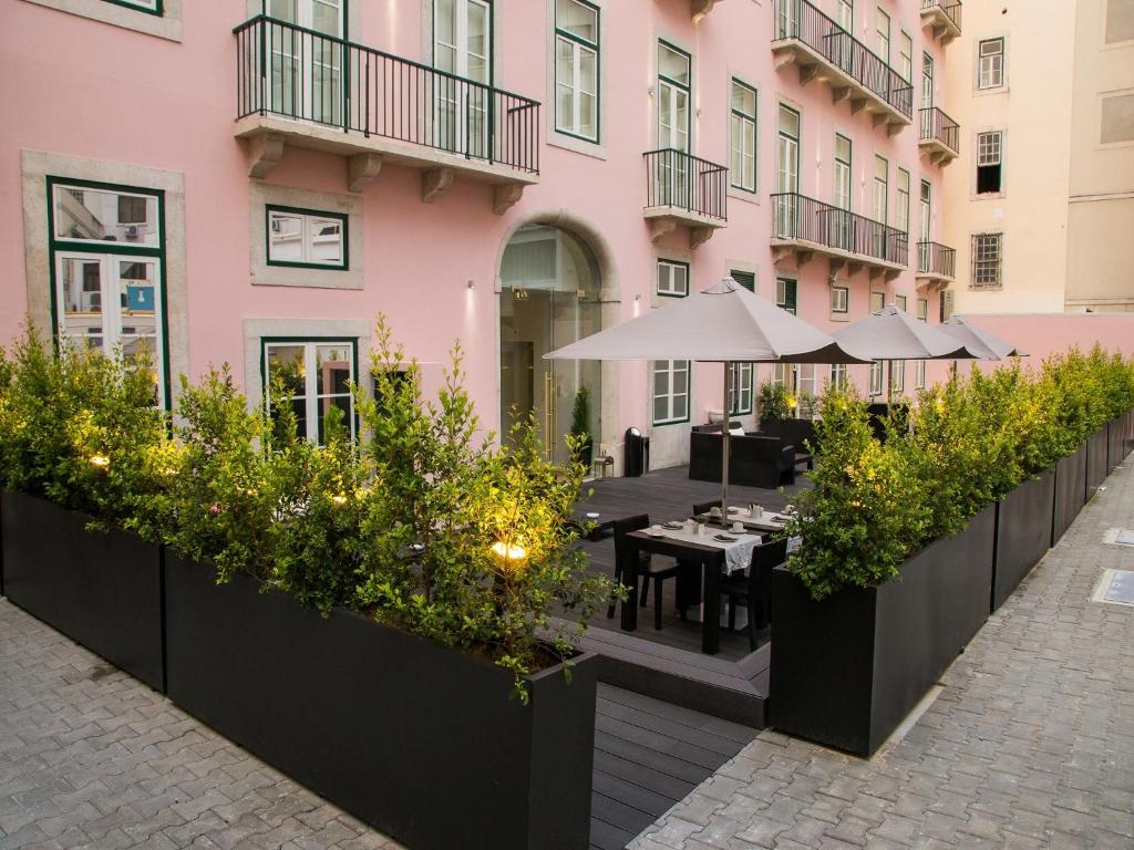 Charming pink building with a stylish outdoor patio, shaded seating, and green bushes in a city setting.
