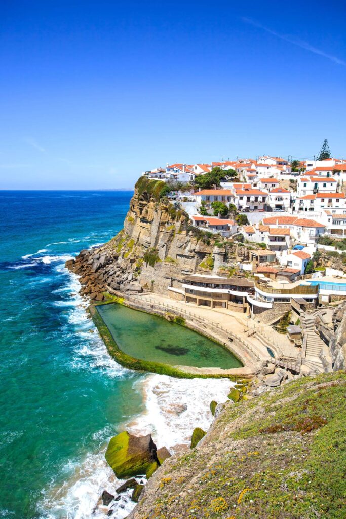 Scenic coastal village on a cliff with ocean view and natural pool under a clear blue sky.