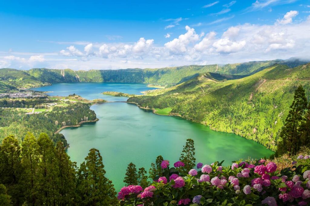 Scenic view of vibrant lagoons and lush green hills with blooming hydrangeas under a blue sky.
